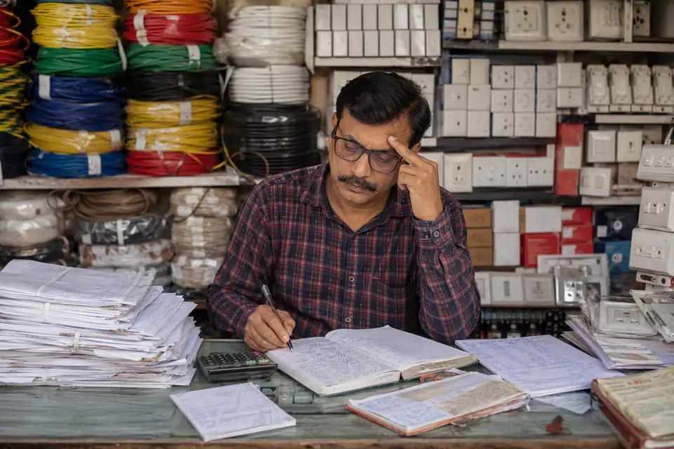 An electrical-goods dealer working through scheme circulars and registers at his counter